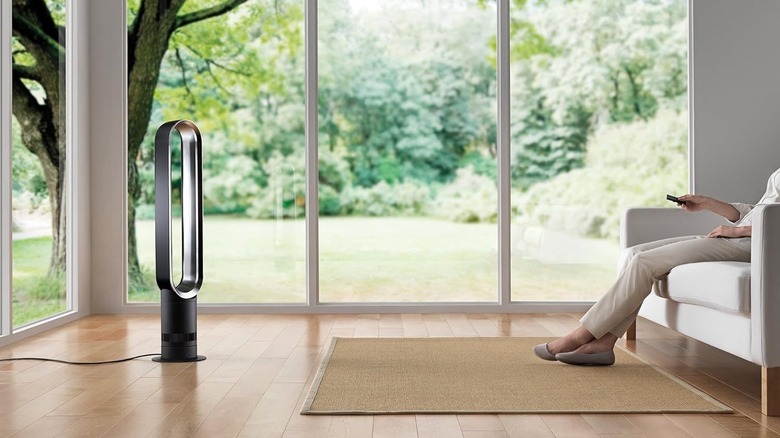 A person sitting on a sofa uses a remote control to adjust the Dyson Cool Tower