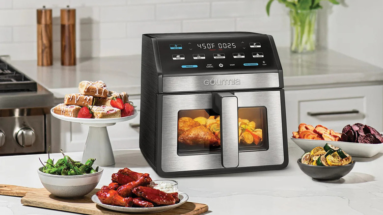 A Gourmia Air Fryer sits on a white kitchen countertop surrounded by food