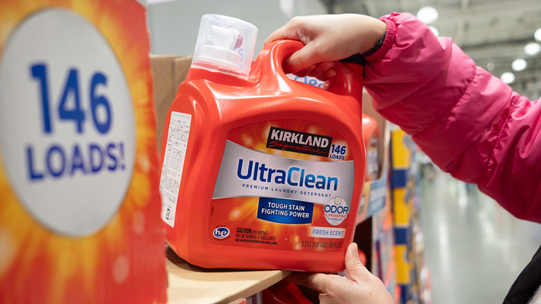 A person lifts Kirkland UltraClean laundry detergent off a store shelf