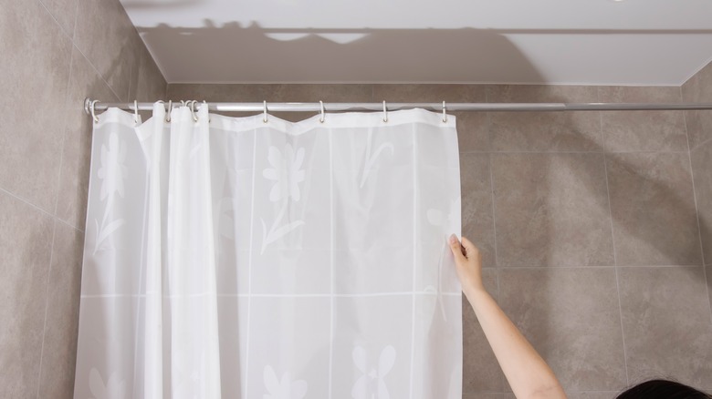 Hand closing a white shower curtain