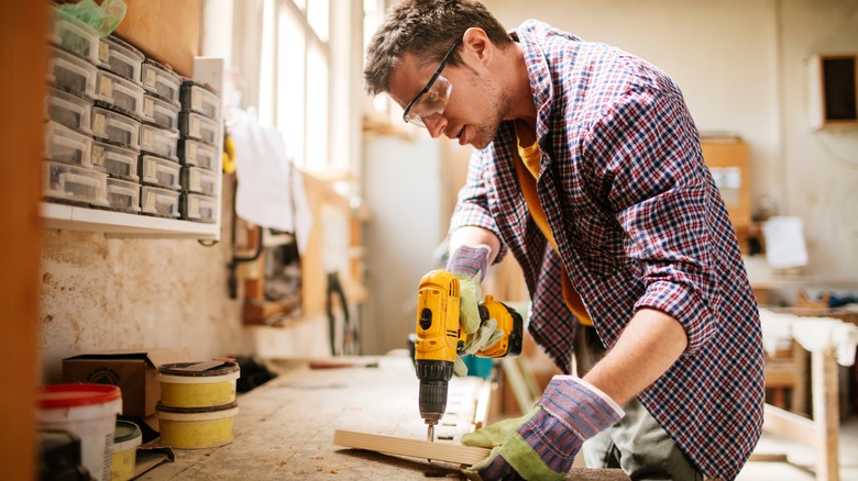 Man drilling hole into piece of wood in workshop