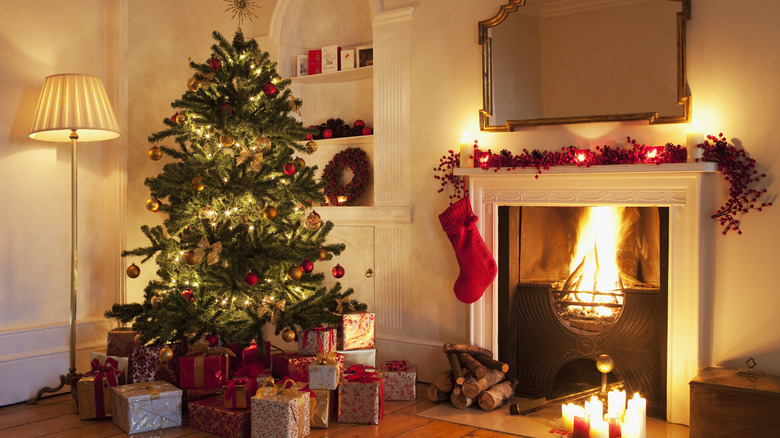 decorated Christmas tree with presents next to lit fireplace