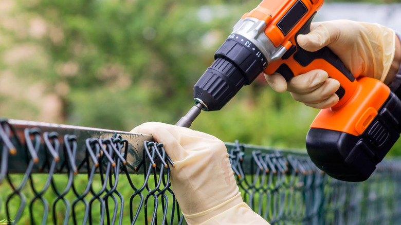 Person fastening metal mesh of chain link fence with screwdriver