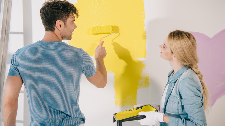 woman holding paint try while partner paints