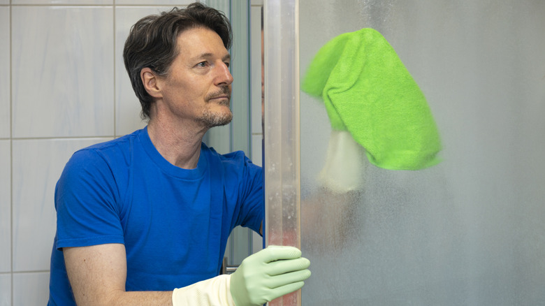 A person wearing gloves wipes down a shower door with a green rag