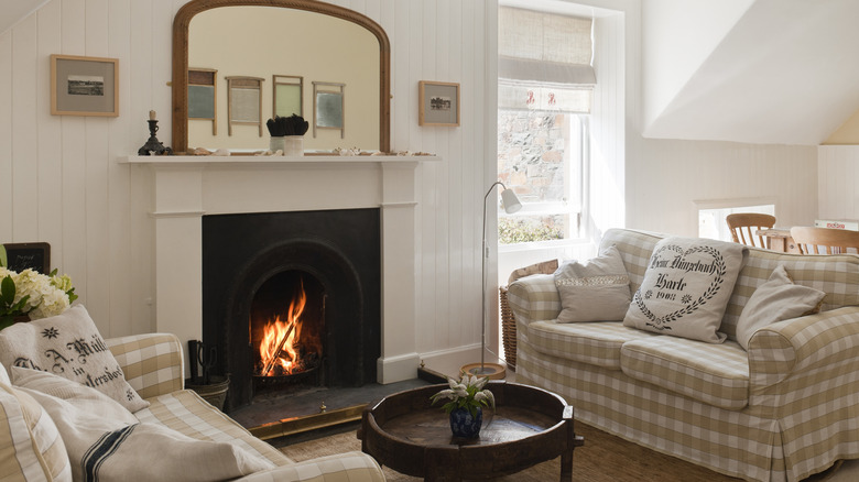 A lit fireplace with two cozy couches on either side and a mirror above the mantel