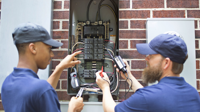 Two workers looking at outdoor breaker box on brick wall