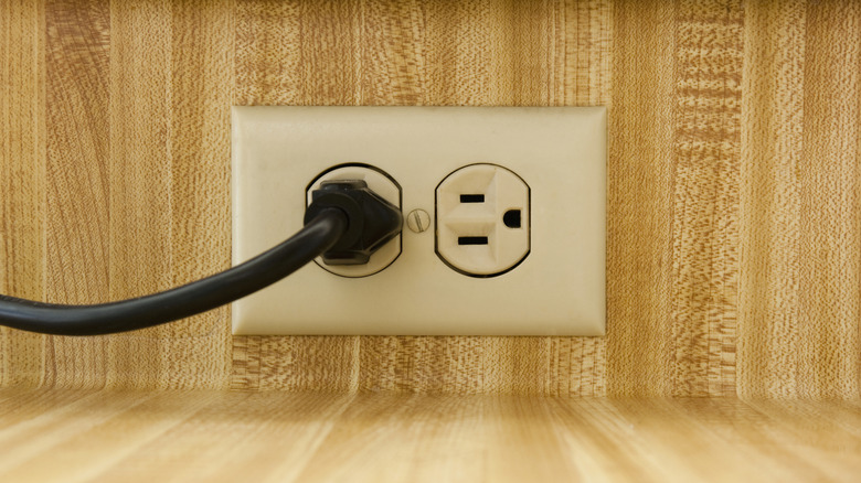 A horizontal outlet on a wooden wall with a black cord plugged in