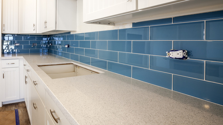 Uncovered horizontal outlets above countertops on a blue kitchen backsplash