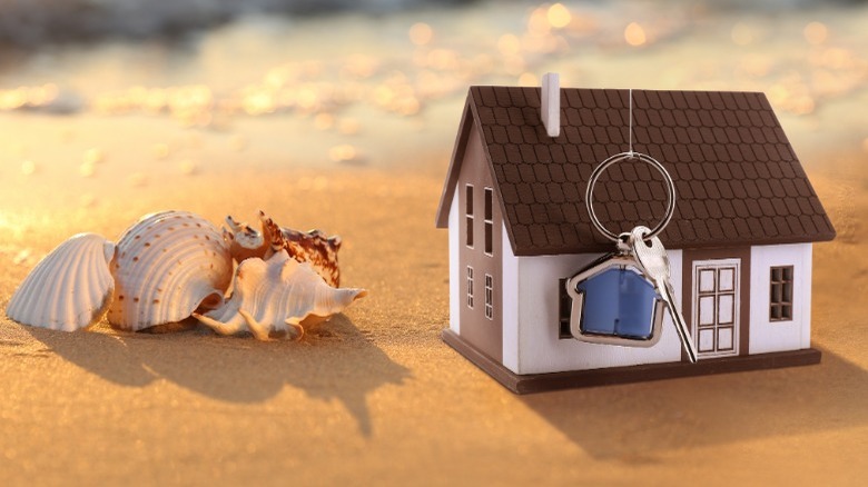 Model of house and keys next to shells on beach