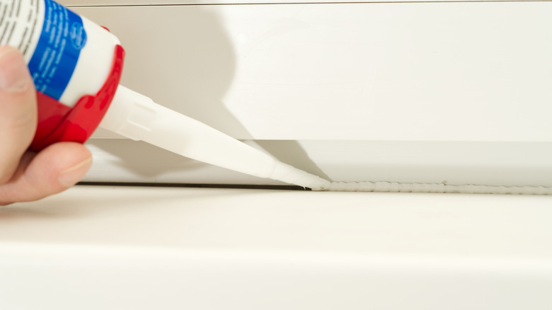 A person squeezes a nozzle to apply sealant to fill in window gaps