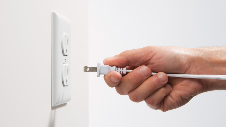 A man's hand plugging a two-prong plug into a three-prong outlet