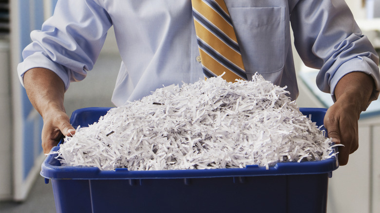 Black person holding a blue recycling bin filled with shredded paper