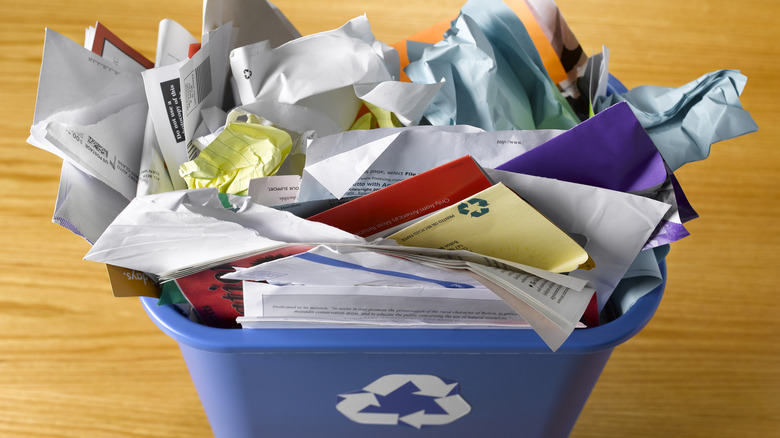 Blue recycling bin overflowing with a wide variety of paper