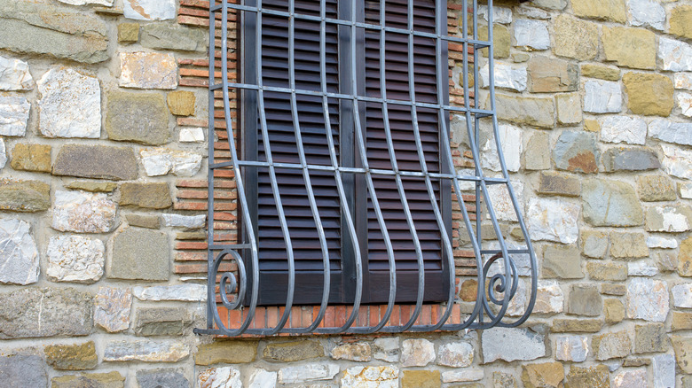 A window on a stone wall is covered by a window grill with a curve at the bottom