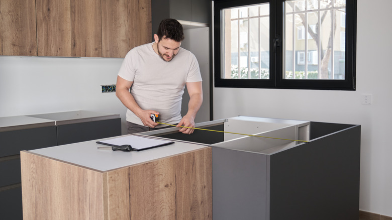 Man measuring cabinets in kitchen to install countertop