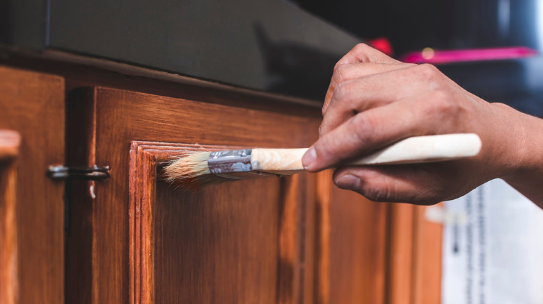 A person applying varnish to cabinets using a small brush