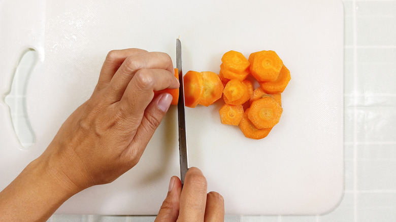 A carrot being chopped on a white plastic cutting board