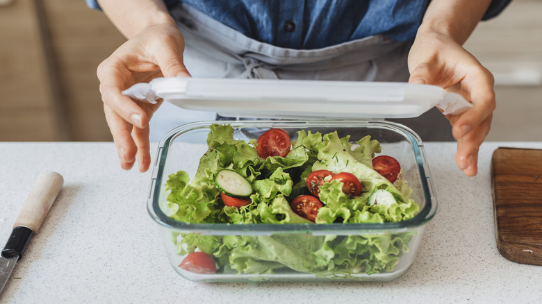 A person storing salad in a glass food container