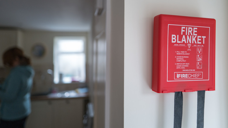 Fire blanket installed on wall with a person cooking in the background