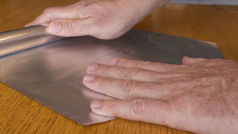 hands unrolling aluminum foil