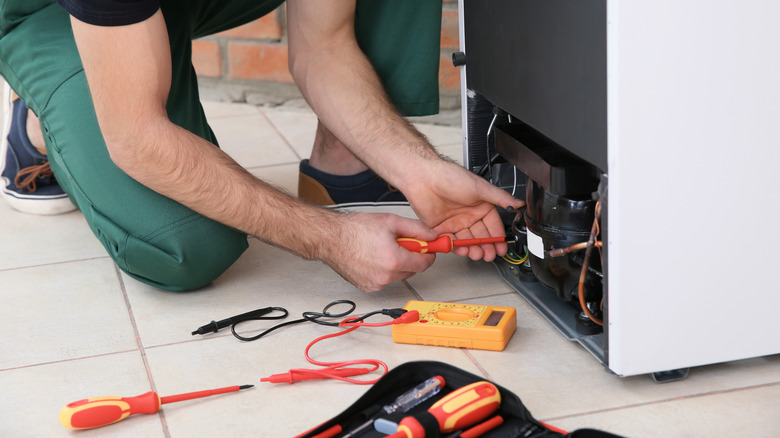 Technician fixing broken refrigerator