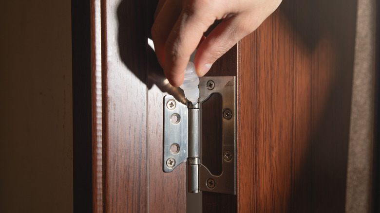 A person is adding a lubricant oil on a door hinge