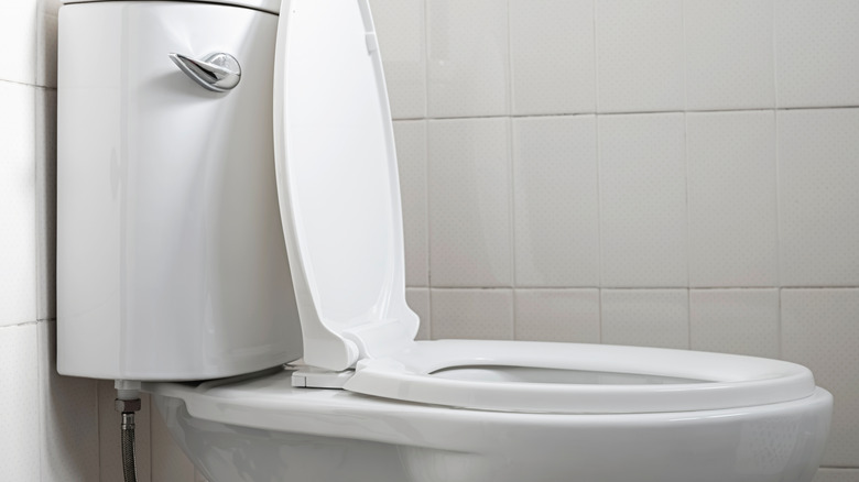 Toilet with its seat up in a bathroom with a tiled wall