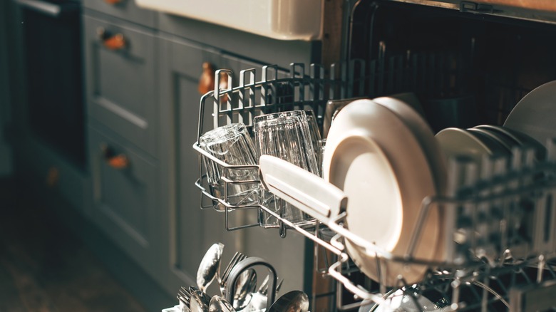 Open dishwasher with racks pulled out full of dishes and glasses