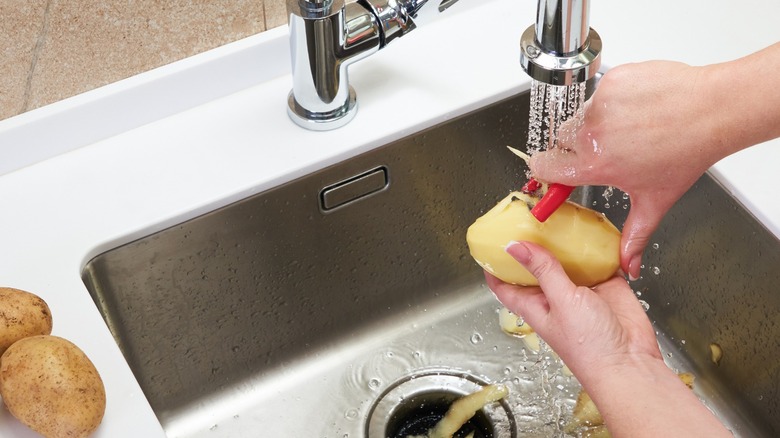 Woman peeling potatoes in sink 