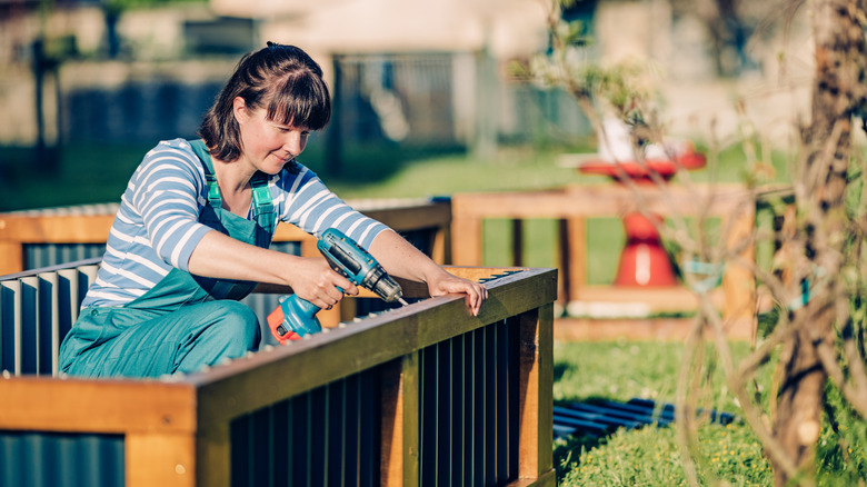 A woman is using a power tool to build a raised garden bed.