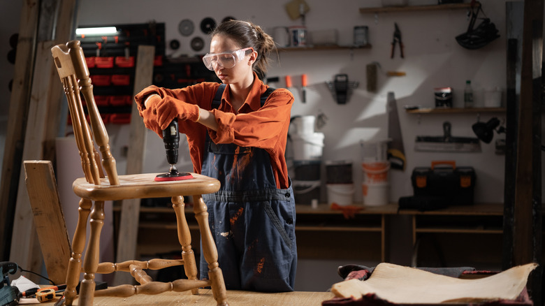 Woman sanding wooden chair in workshop