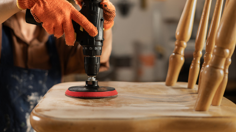 female carpenter wearing orange gloves and sanding an old wooden chair