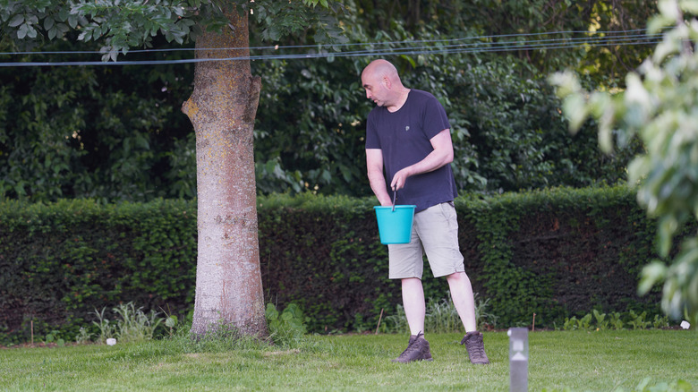 Man holding a blue bucket of fertilizer for his lawn