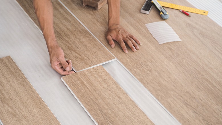 Person installing vinyl floor tiles after using a cutter, ruler and pencil to cut them