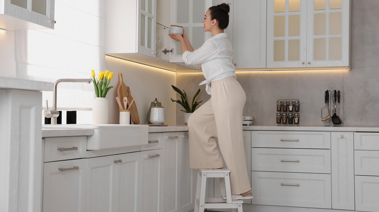 woman on a step ladder to reach cabinet