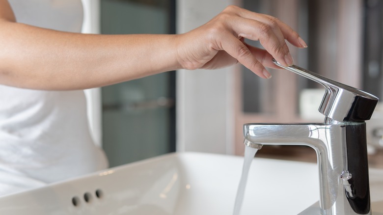 Hand touching bathroom sink faucet