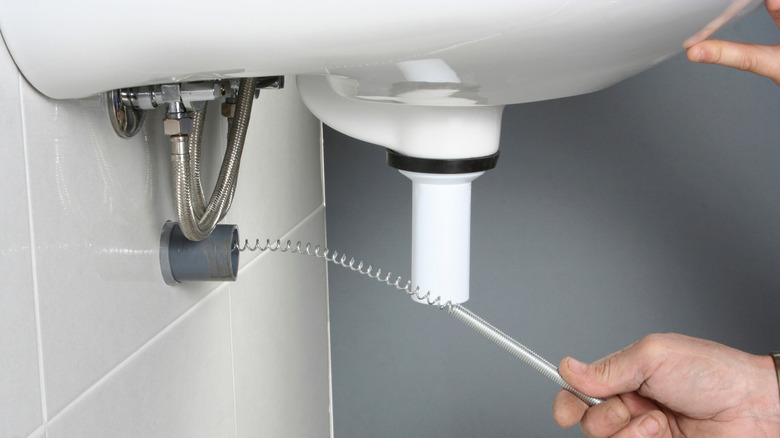 Person using a drain snake to clean a sink.