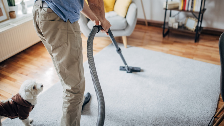 Man vacuuming rug near dog