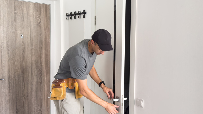 A man installs a new door in a white room