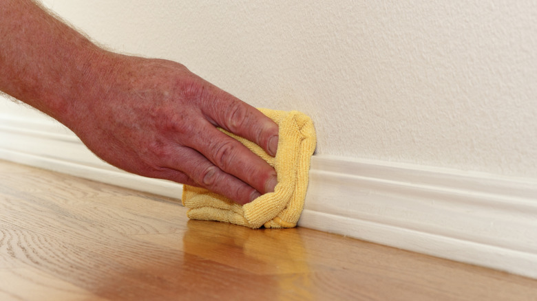 Person cleaning baseboards with cloth