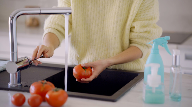 Woman holding tomato over sink