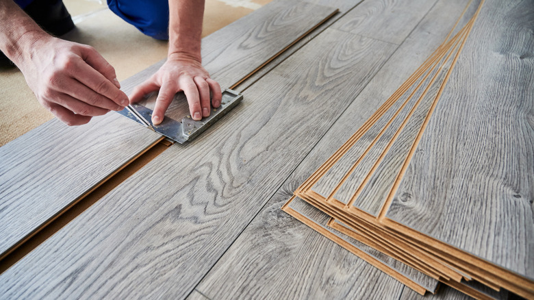 Man using metal tool and pen to mark laminate flooring plank