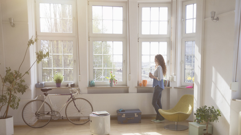 A woman stands next to large windows that flood a room with natural light