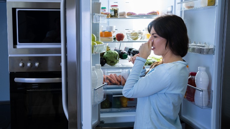 Woman holding nose in front of stinky fridge