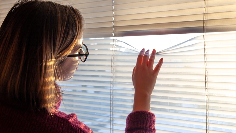 woman looking out window blinds