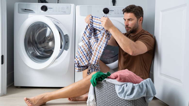 A person sits on the floor in laundry room holding a shirt