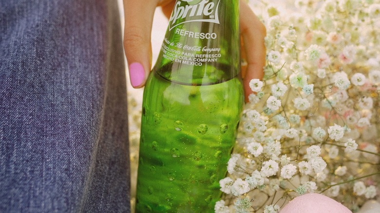 hand holding Sprite beside flowers