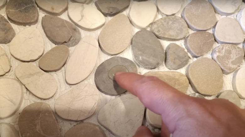 man pointing at water pooling on pebble shower floor