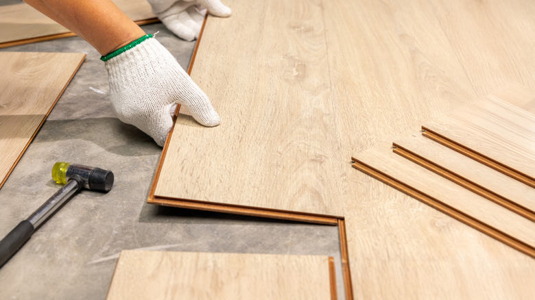 Hands wearing white gloves and installing interlocking laminate floorboards